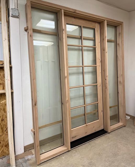 Wood-framed glazed door with rectangular glass divisions and a sidelight on each side, photographed in a workshop