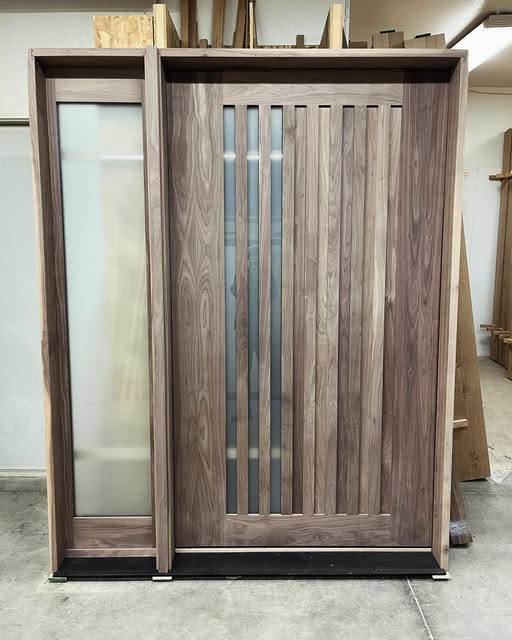 Wood door with narrow vertical glass openings and a tall sidelight, photographed in a workshop